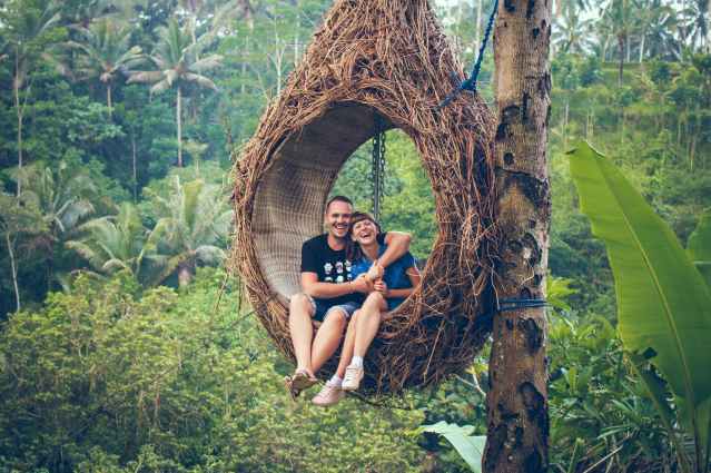 man and woman sitting on hanging chair by a tree